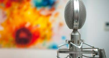 A close-up of a vintage microphone on a stand, set against a colorful abstract background of orange, blue, and yellow hues.