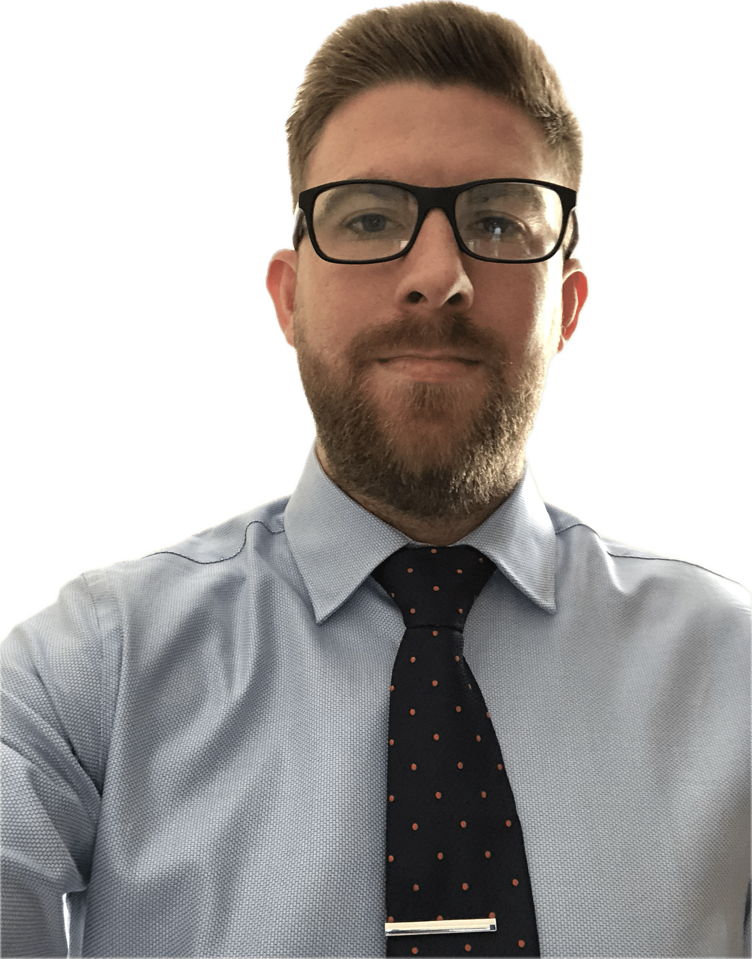 A man with short hair and a beard wears glasses, a light blue dress shirt, and a dark tie with polka dots, looking directly at the camera.