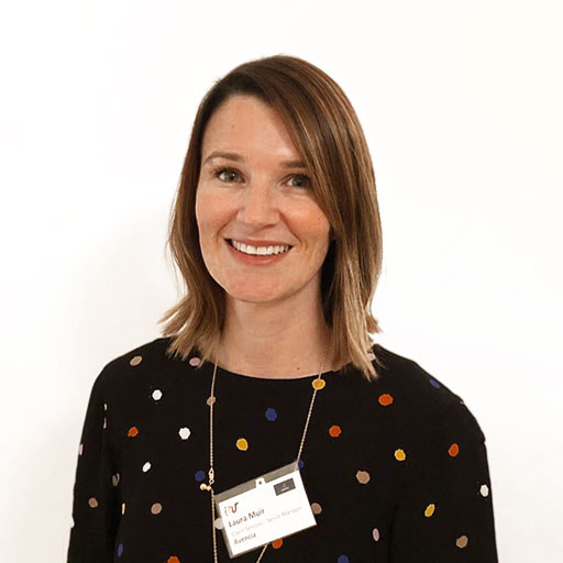 A smiling woman with medium-length brown hair, wearing a black dress with colorful polka dots. She has a name tag around her neck and stands against a plain white background.