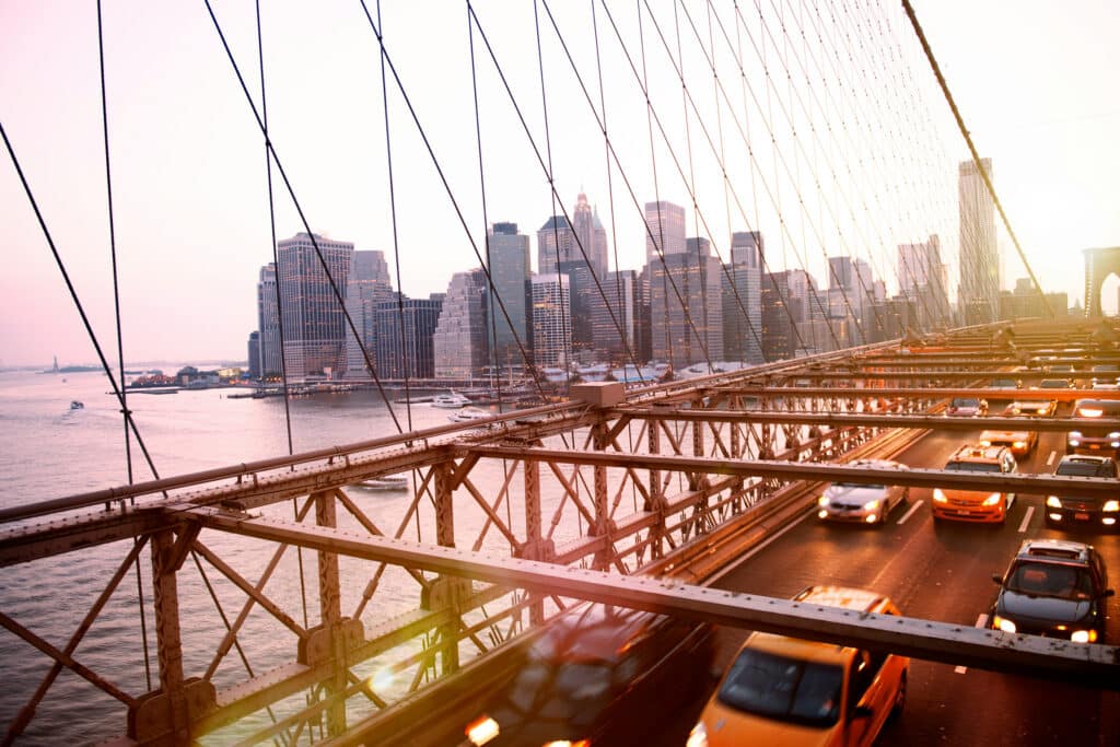 View of the Brooklyn Bridge with traffic and the Manhattan skyline during a warm, glowing sunset.